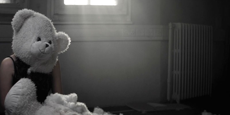 Woman Sitting In Derelict Room Surrounded By Wool With Teddy Bear Mask