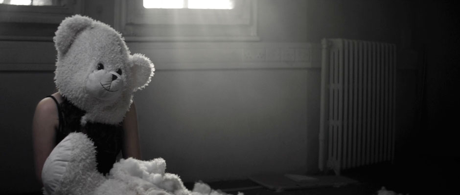 Woman Sitting In Derelict Room Surrounded By Wool With Teddy Bear Mask