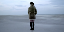 Cinematic music video production shot featuring a stylized performance scene of a female singer on a scenic beach backdrop.