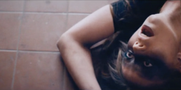 Cinematic music video production still featuring an intense, moody narrative scene with a female artist on a bathroom floor.