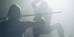 cinematic music video production shot showcasing an action-packed narrative scene with martial artists executing a stylized stick fight.