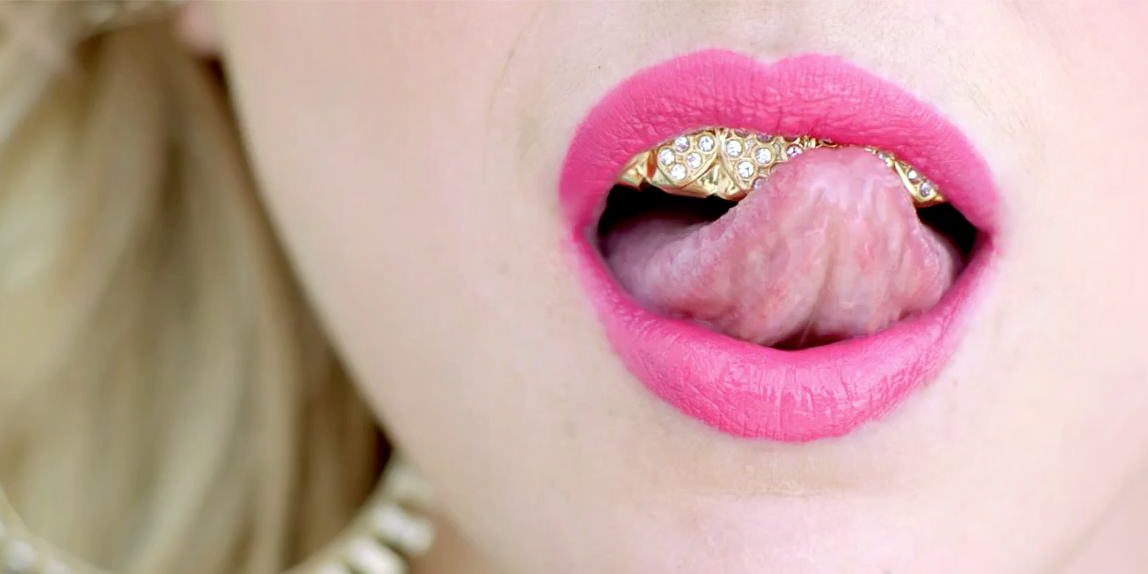 Female Model With Pink Lipstick Blonde Hair Gold Earrings And Tongue Licking Diamond Teeth Grill