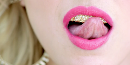 Cinematic music video production shot featuring a stylized close-up performance scene of a woman with a diamond teeth grill.