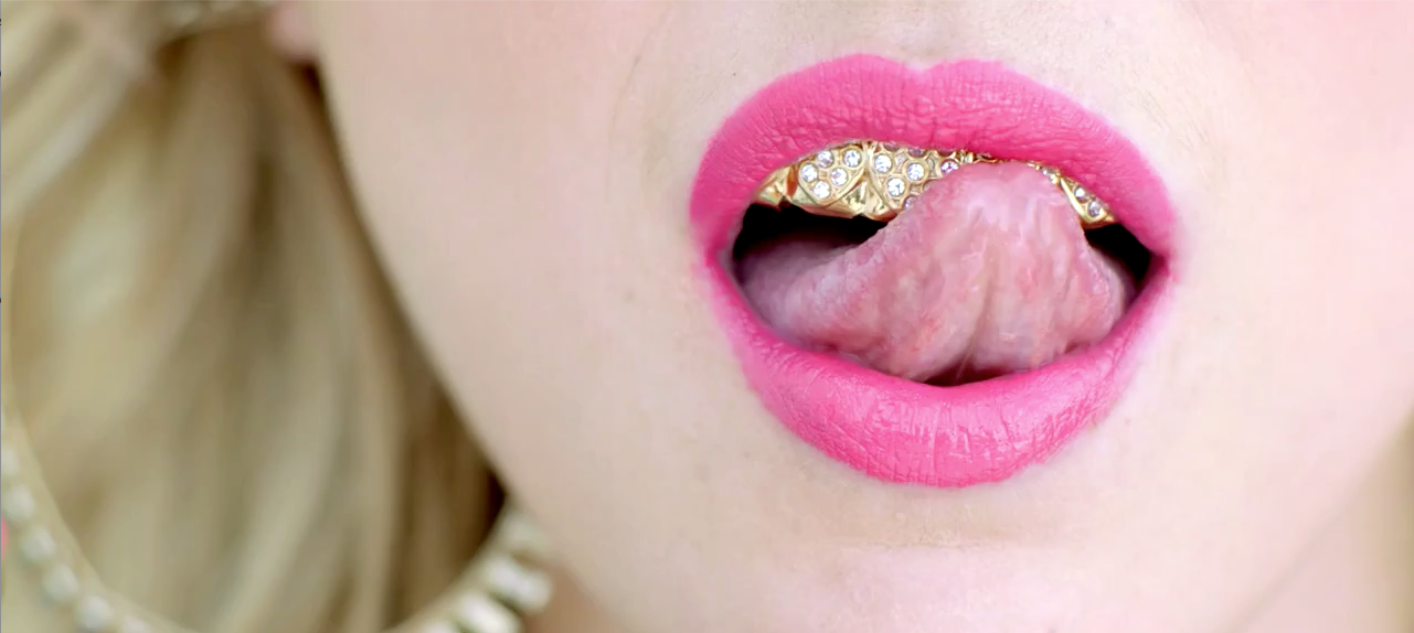 Female Model With Pink Lipstick Blonde Hair Gold Earrings And Tongue Licking Diamond Teeth Grill
