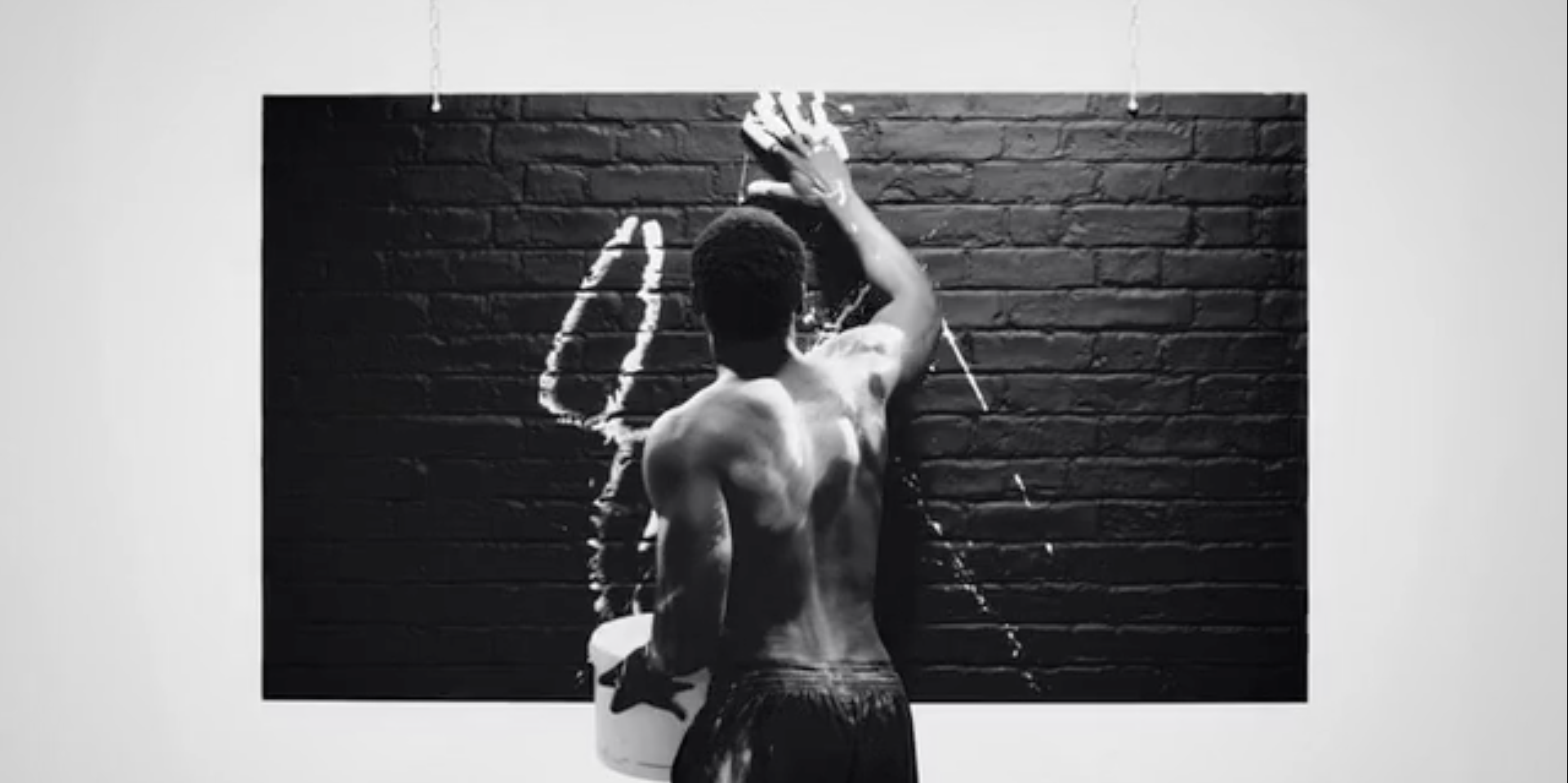 Man Standing In Studio Covered In White Paint Smudges A Black Brick Wall