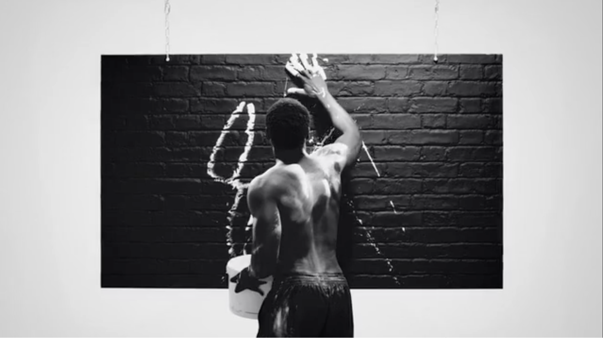 Man Standing In Studio Covered In White Paint Smudges A Black Brick Wall