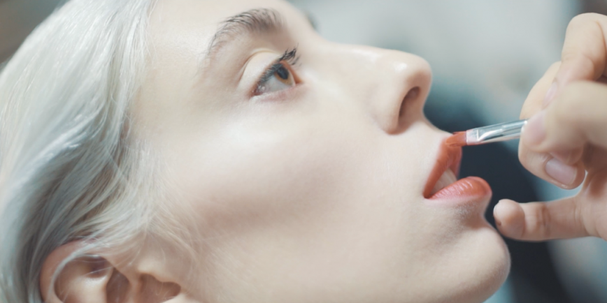 Beautiful Female Model With Brown Eyes And Grey Hair Having Lipstick Applied By Makeup Artist At Fashion Runway Show