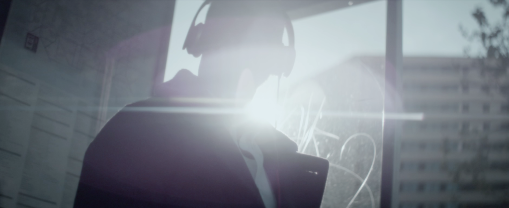 Man Standing At Bus Stop Wearing Headphones With Bright Flare Background