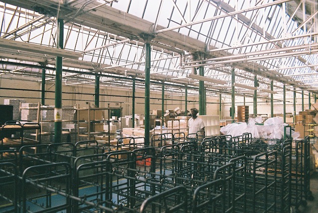 Professional Photography Black Man With Traditional Hat Walking Through Empty Grenson Shoe Factory Surrounded By Metal Racks