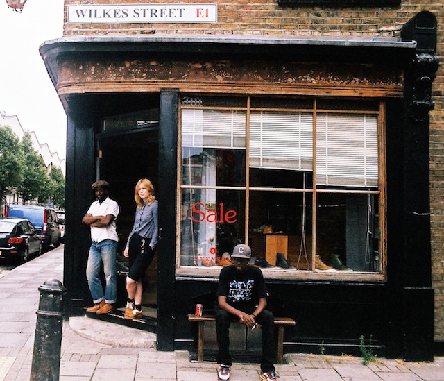 Professional Photography Black Man Sitting Outside Of Grenson Shoe Store Wearing Bathing Ape With Two People In Doorway In Brick Lane Wilkes Street