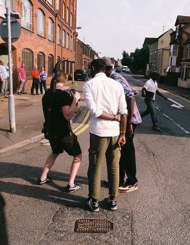 Professional Photography Black Man White Man And Asian Man Filming Outside Of Grenson Shoe Factory With Small Crowd Watching