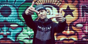 Professional Photography Black Man Wearing Black Hat And Hashtagee Generals Streetwear Hoodie Standing In Front Of Colourful Graffiti Mural Showing Two Middle Fingers