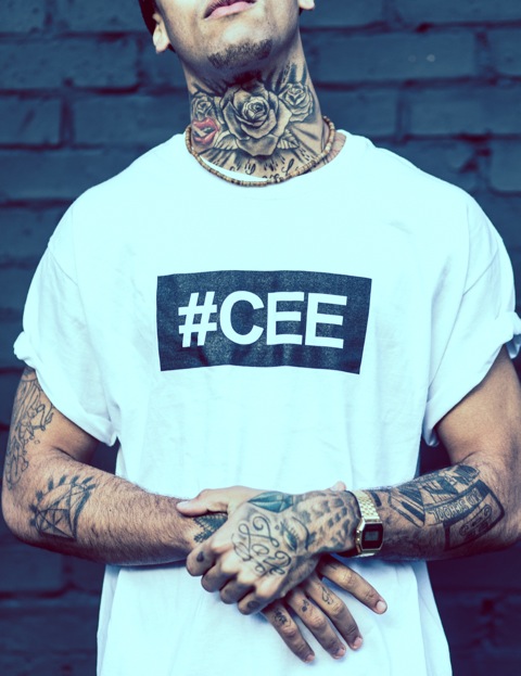 Professional Photography Close-Up Of Black Man With Tattoos In Front Of Black Brick Wall Wearing White Hashtagcee Generals T-Shirt