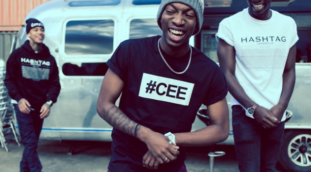 Professional Photography Black Man In Black Hashtagcee T-Shirt Laughing Being Followed By Two Black Men Wearing Hashtagcee Generals White T-Shirt And Generals Black Hoody