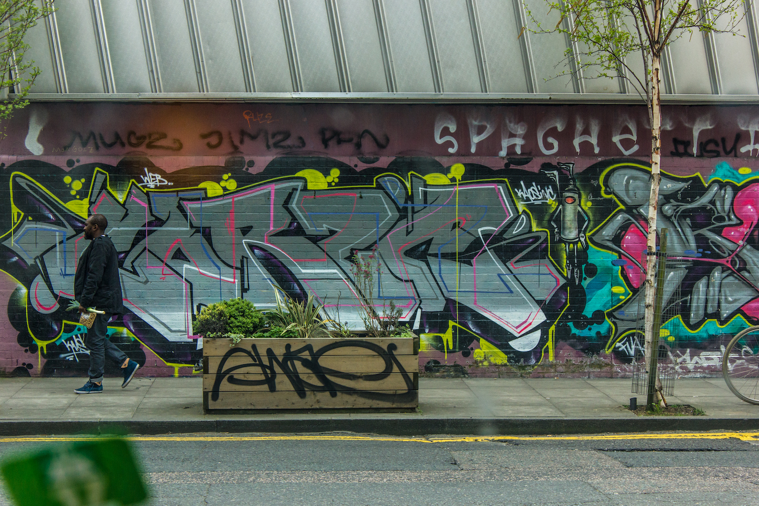 Professional Photography Black Man In Blazer Walking With Bag In Front Of Graffiti Mural In Shoreditch East London