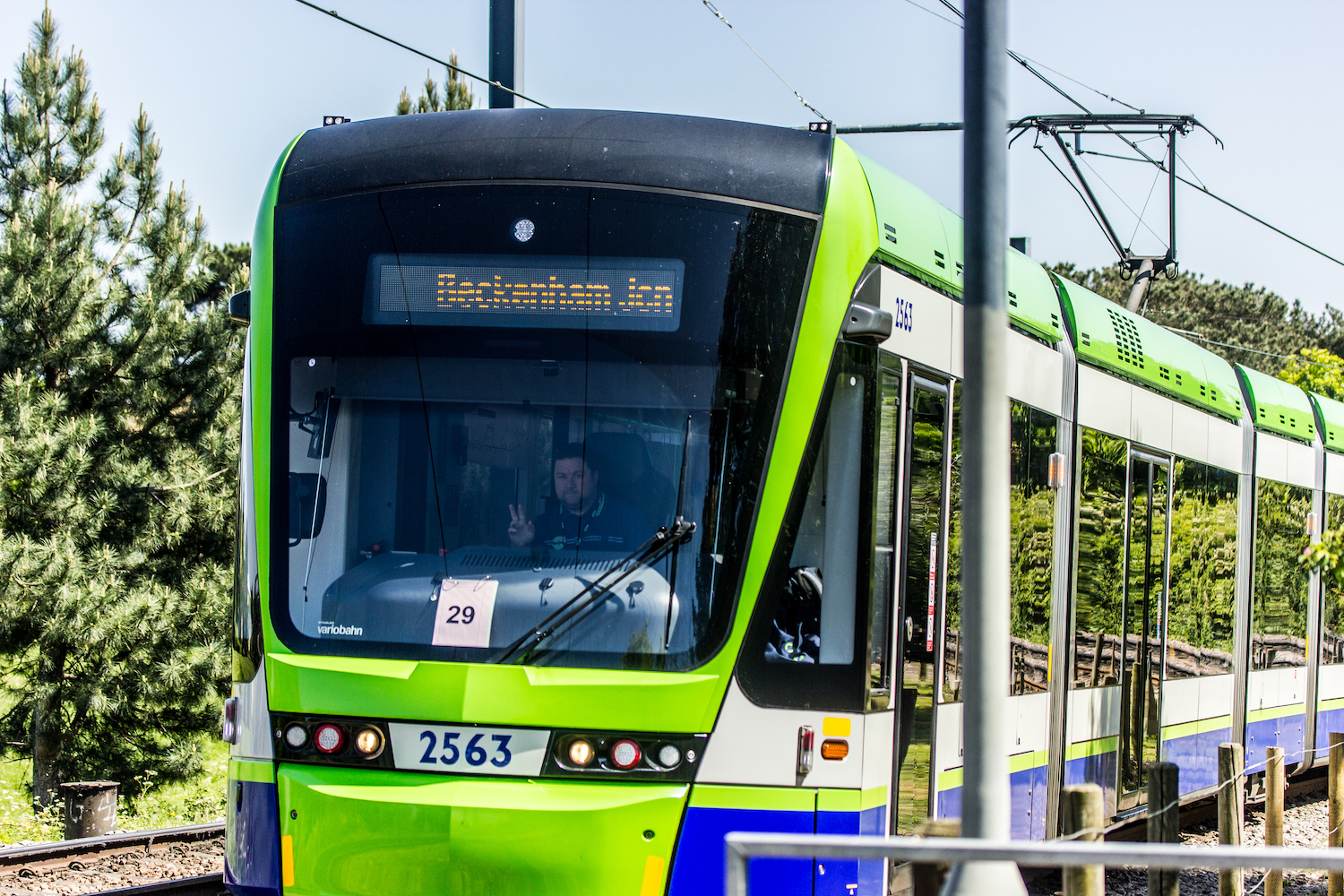 Professional Photography Male Tram Driver Approaches Giving Peace Sign While Driving Surrounded By Trees And Nature In South Norwood South London