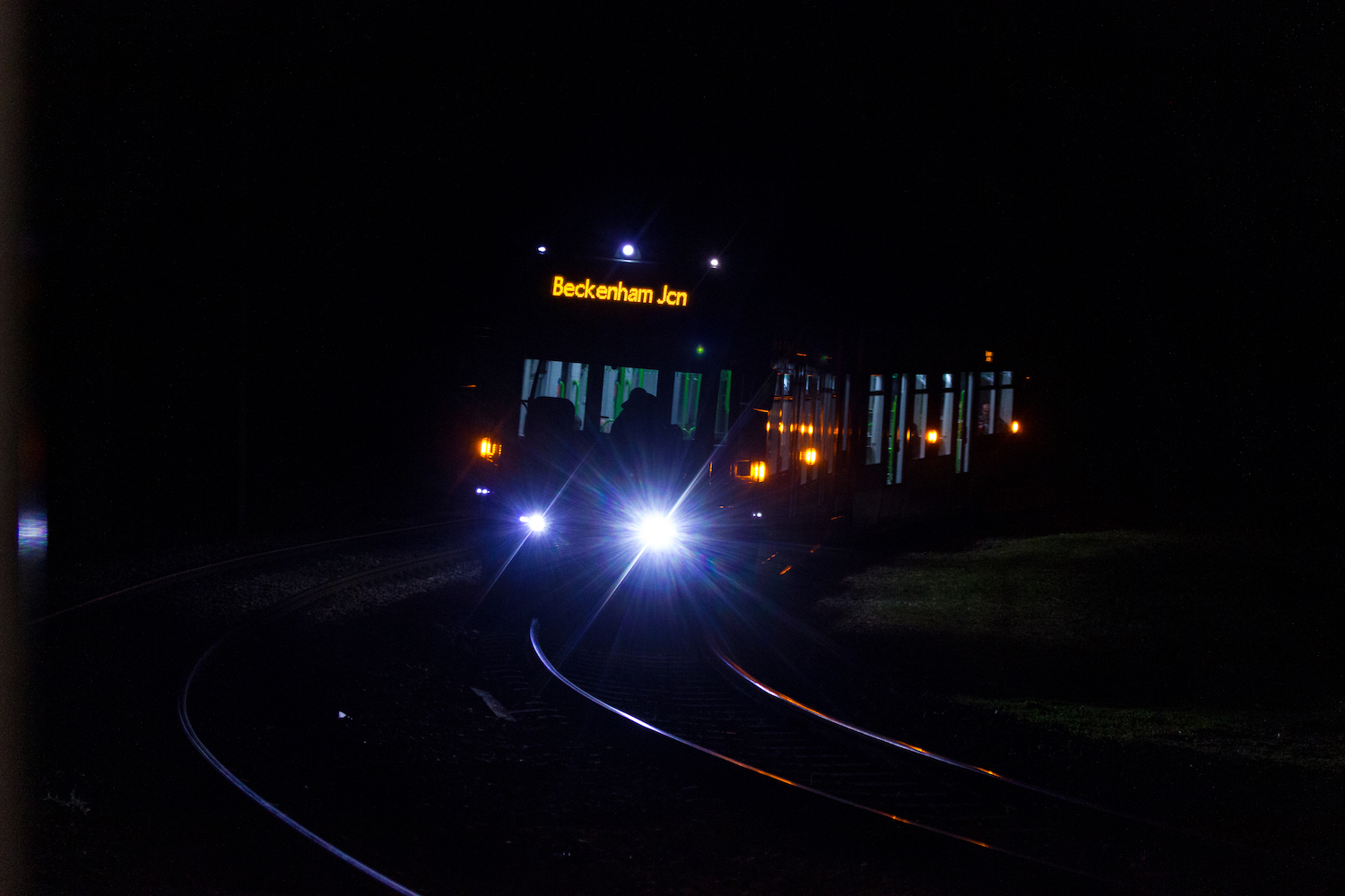 Professional Photography Tram Train At Night In Shadows With Extremely Bright Headlights Coming Around Bend In South Norwood London