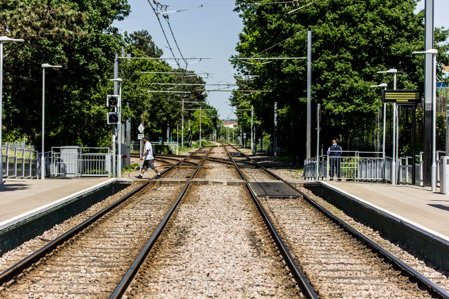 Professional Photography One Man Waits While Another Crosses The Tram Tracks Surrounded By Green Trees In South Norwood South London