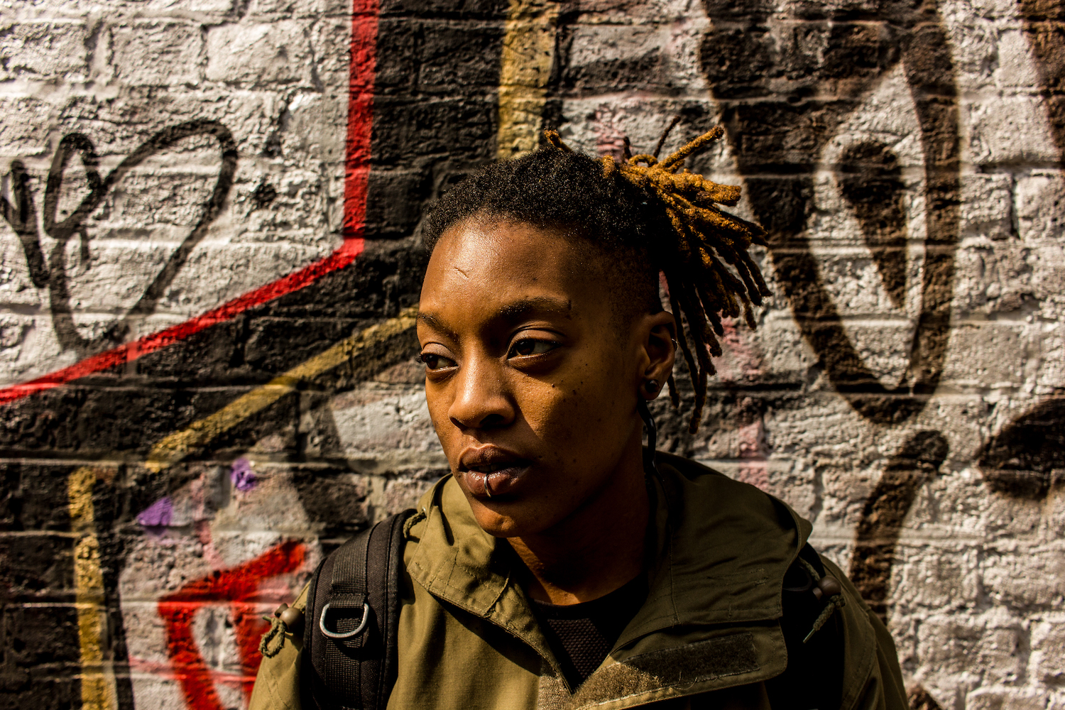 Professional Photography Black Woman With Lip Ring Khaki Jacket Black Backpack And Dreadlocks Standing In Front Of Graffiti Wall Near Little Venice Paddington London