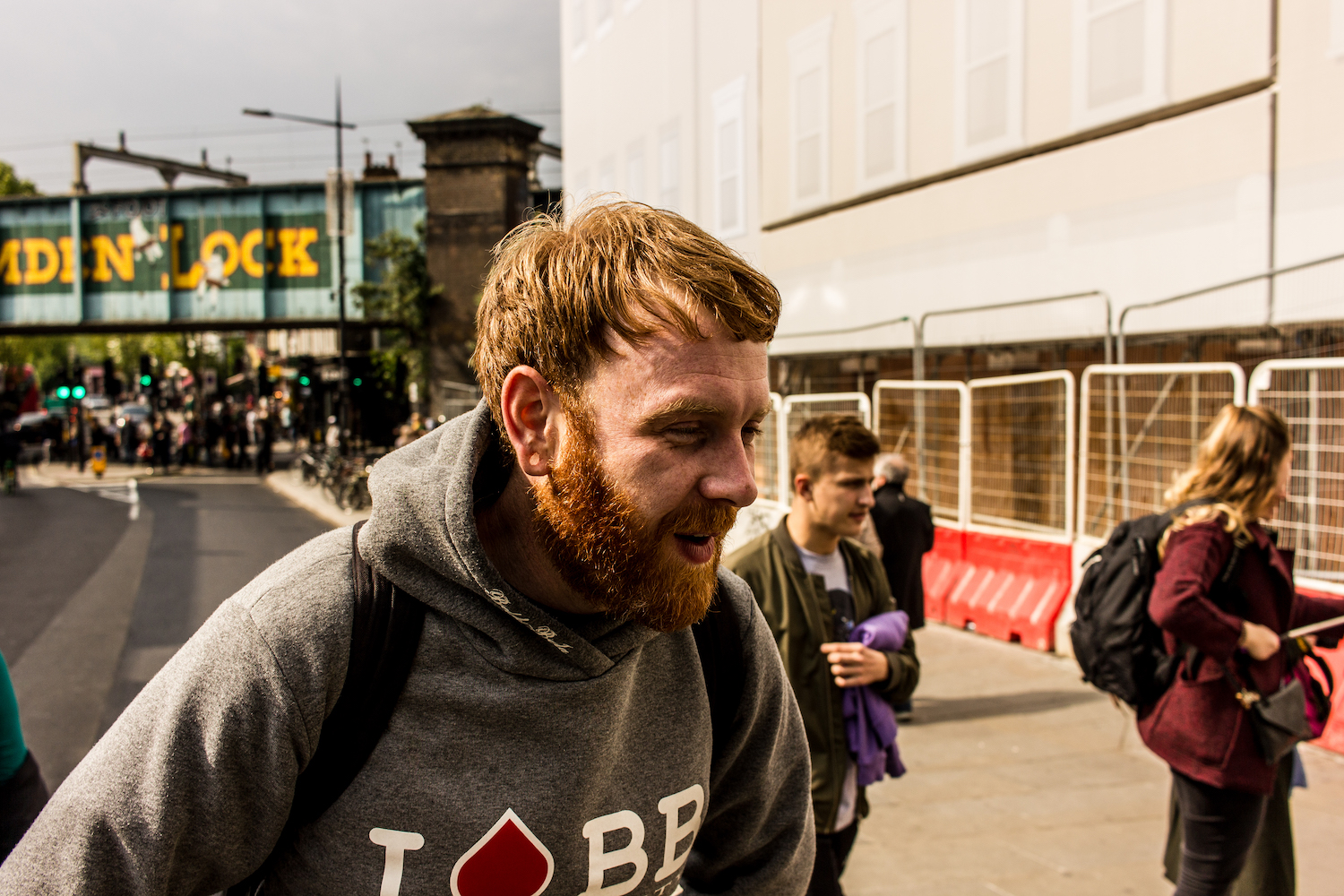 Professional Photography White Man With Beard In Grey Hoody Black Jeans And Backpack Exhausted In Front Of Bridge In Camden Town