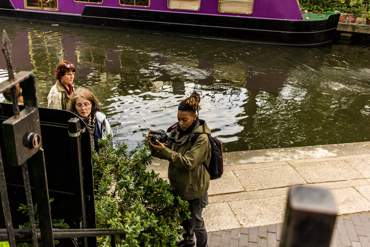 Professional Photography Black Woman In Khaki Jacket And Black Backpack Next To Canal River And Boats Filming With Camera In Little Venice Paddington London