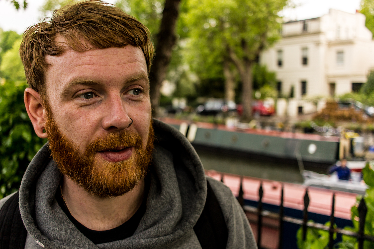 Professional Photography White Man With Beard Standing Under Green Trees Beginning Ten Mile Charity Walk In Grey Hoody With Canal River And Boats In Background In Little Venice Paddington London