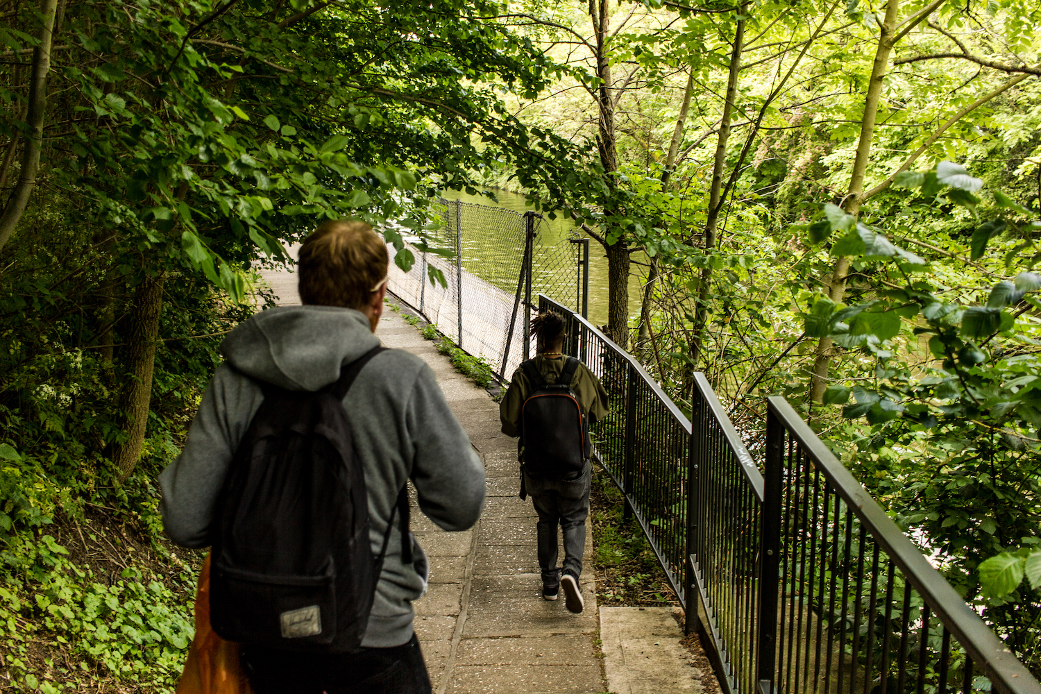 Professional Photography White Man In Grey Hoody Black Jeans And Backpack Walking Down Pathway With Black Woman With In Khaki Jacket Dreadlocks And Black Backpack Walking In Little Venice Paddington London Next To Canal River