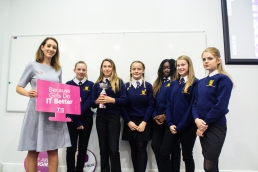 Professional Photography Six Female Students In Blue Sweatshirts Holding Silver And Pink Trophy At Event With Woman In Grey Dress