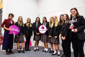 Professional Photography Nine Award Winning Female Students Wearing Black Blazers Holding Trophy And Banners At Event With Woman In Blue Dress