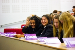 Professional Photography Two Female Students Wearing Blue Blazers Smiling At Camera In Front Row Of Event One Holding Fingers In Peace Sign