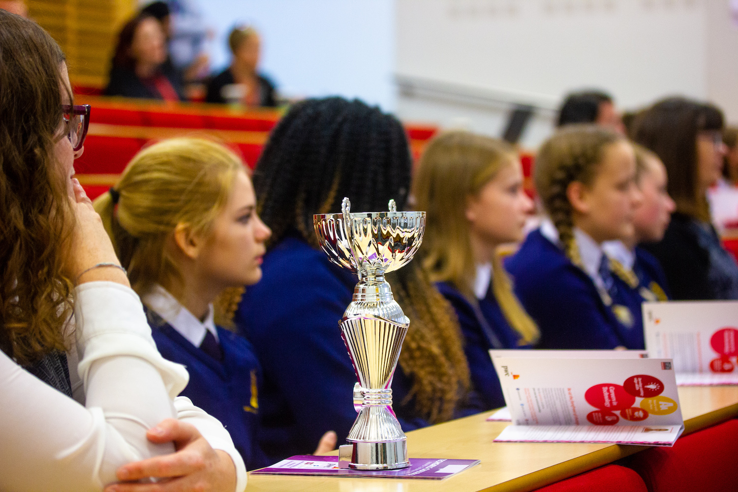 Professional Photography Silver Trophy With Female Students Wearing Blue Sweatshirts In Row Watching Event