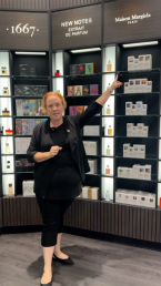 woman standing in The Fragrance Shop in Bluewater Kent, pointing at the perfume maison margiela and jimmy choo